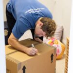 A man wearing a blue polo shirt writing descriptions in a box